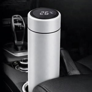 Witte thermosfles met digitale temperatuurmeter in zwarte dop, geplaatst in de bekerhouder van een auto.